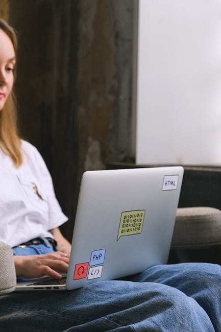 A laptop computer with a black keyboard displaying lines of code on a blurred screen, placed on a dark surface next to a white Puma cap featuring the brand's logo. The scene appears to be indoors, wit